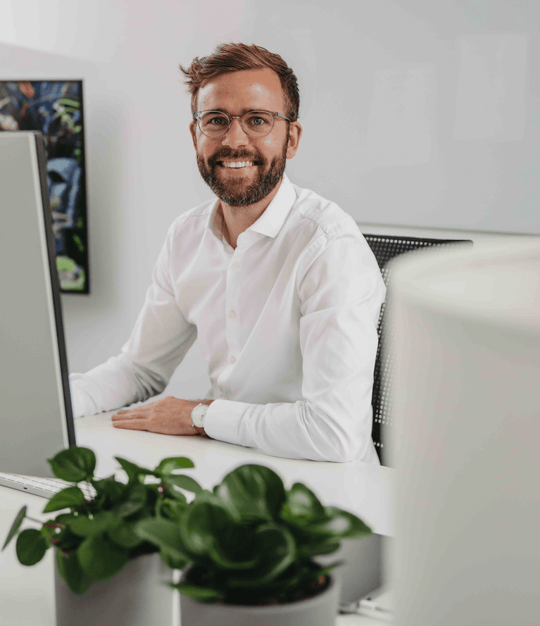 Tim Schmaddebeck lächelnd am Schreibtisch in seinem Büro in Hamburg