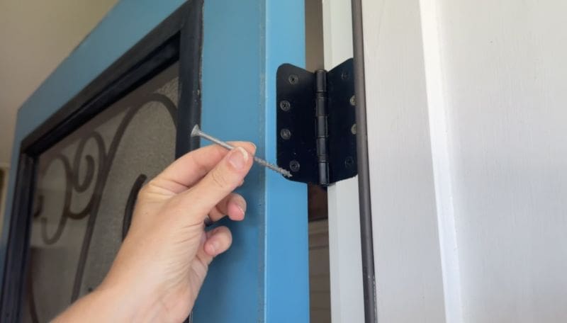 Screenshot Door Details 6 Things To Know About Doors MyFixitUpLife MyFixitUpLife Person holding a long screw near a door hinge on a blue frame about to install or adjust it MyFixitUpLife
