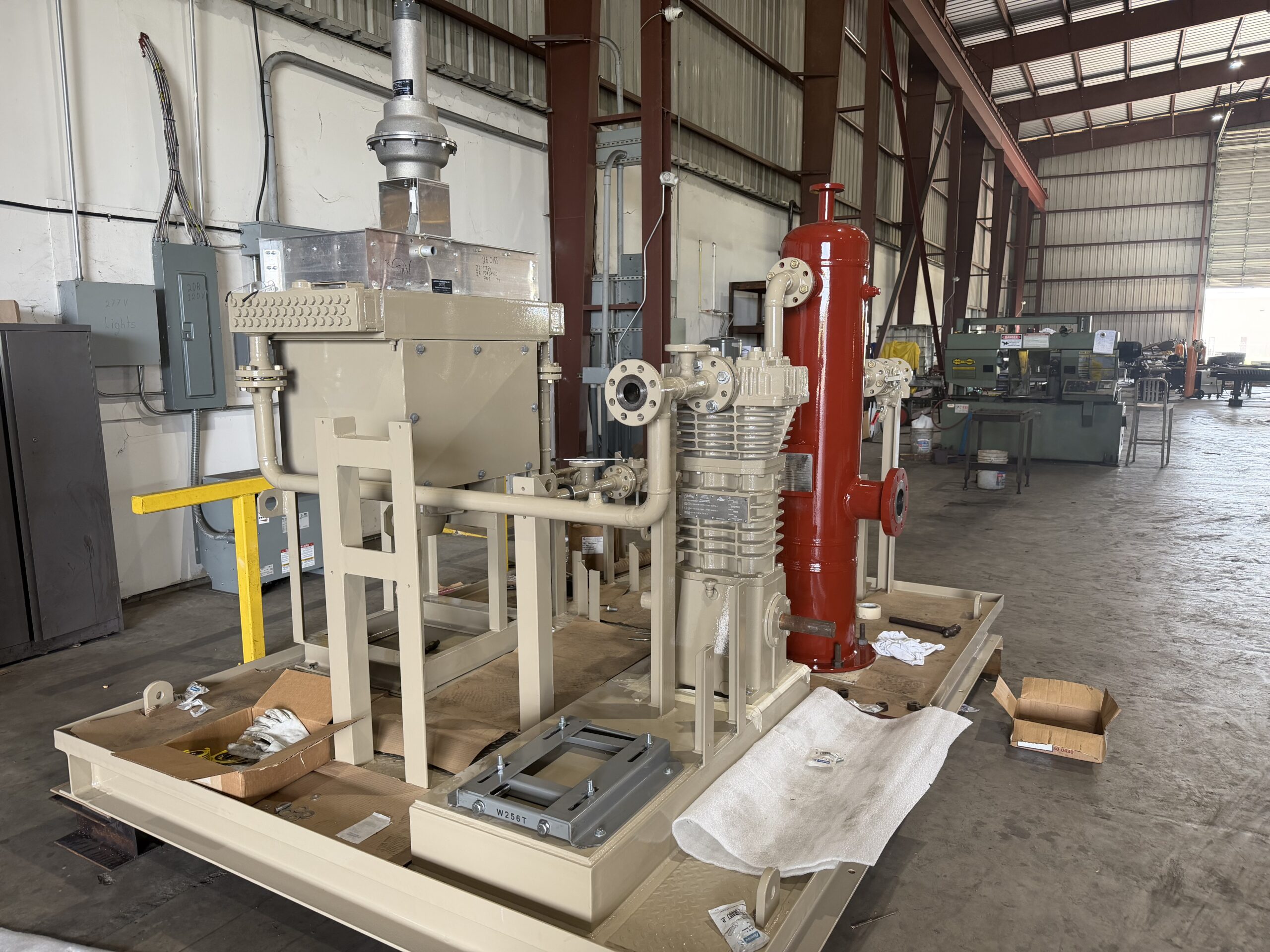 Custom-fabricated natural gas compressor skid package with reciprocating compressor, red vertical separator vessel, and integrated piping at WeldIT's Houston fabrication shop