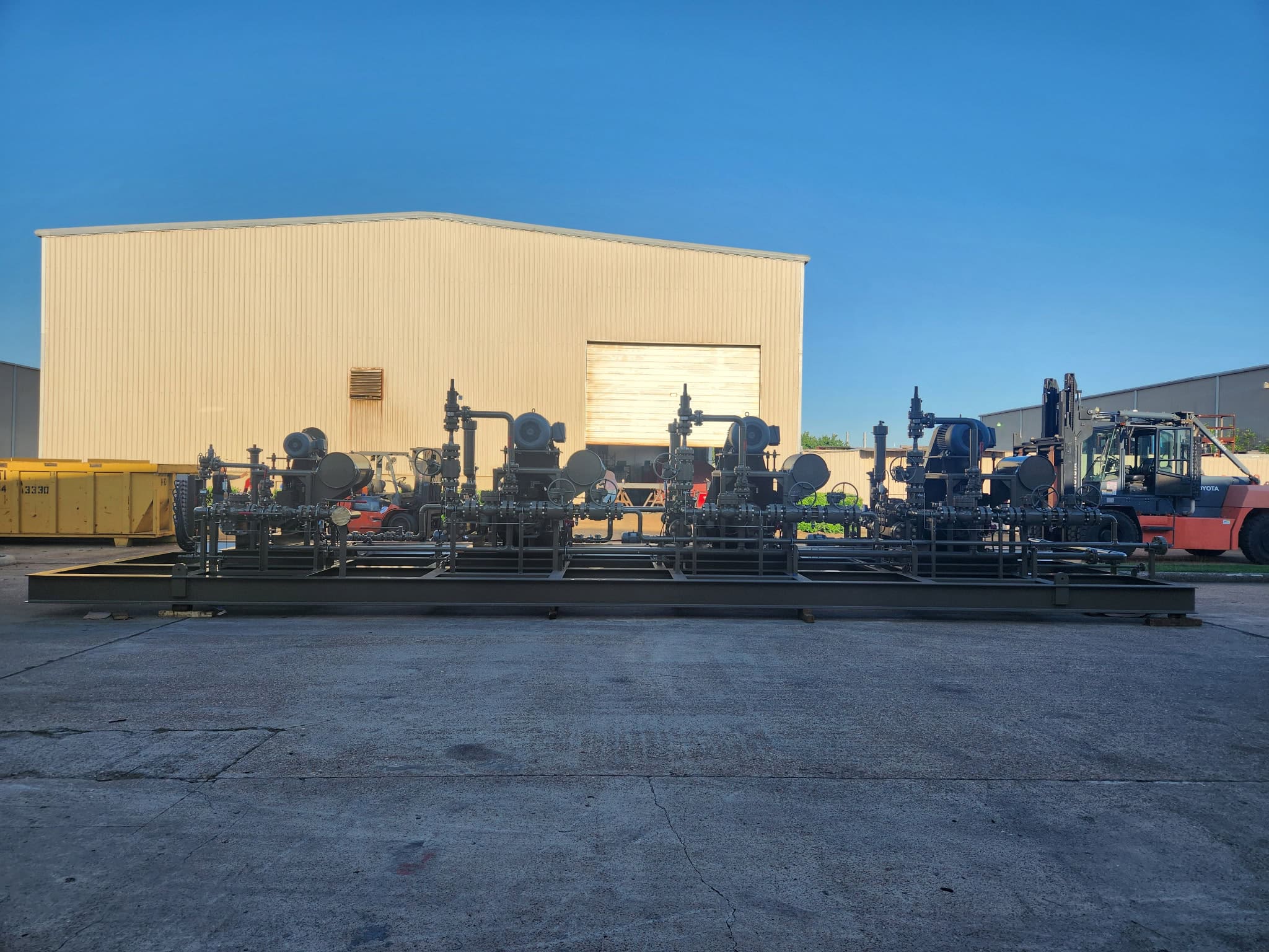 Complete multi-pump process skid package on a structural steel base outside the WeldIT fabrication shop with a forklift in the background