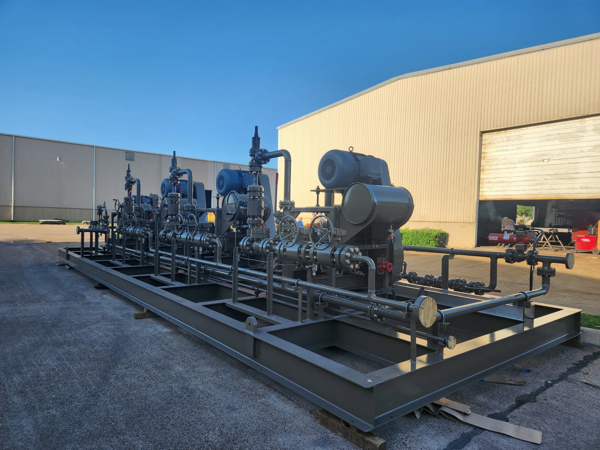 Side view of a multi-pump process skid with several pump and motor sets, piping headers and valves on a long structural steel base