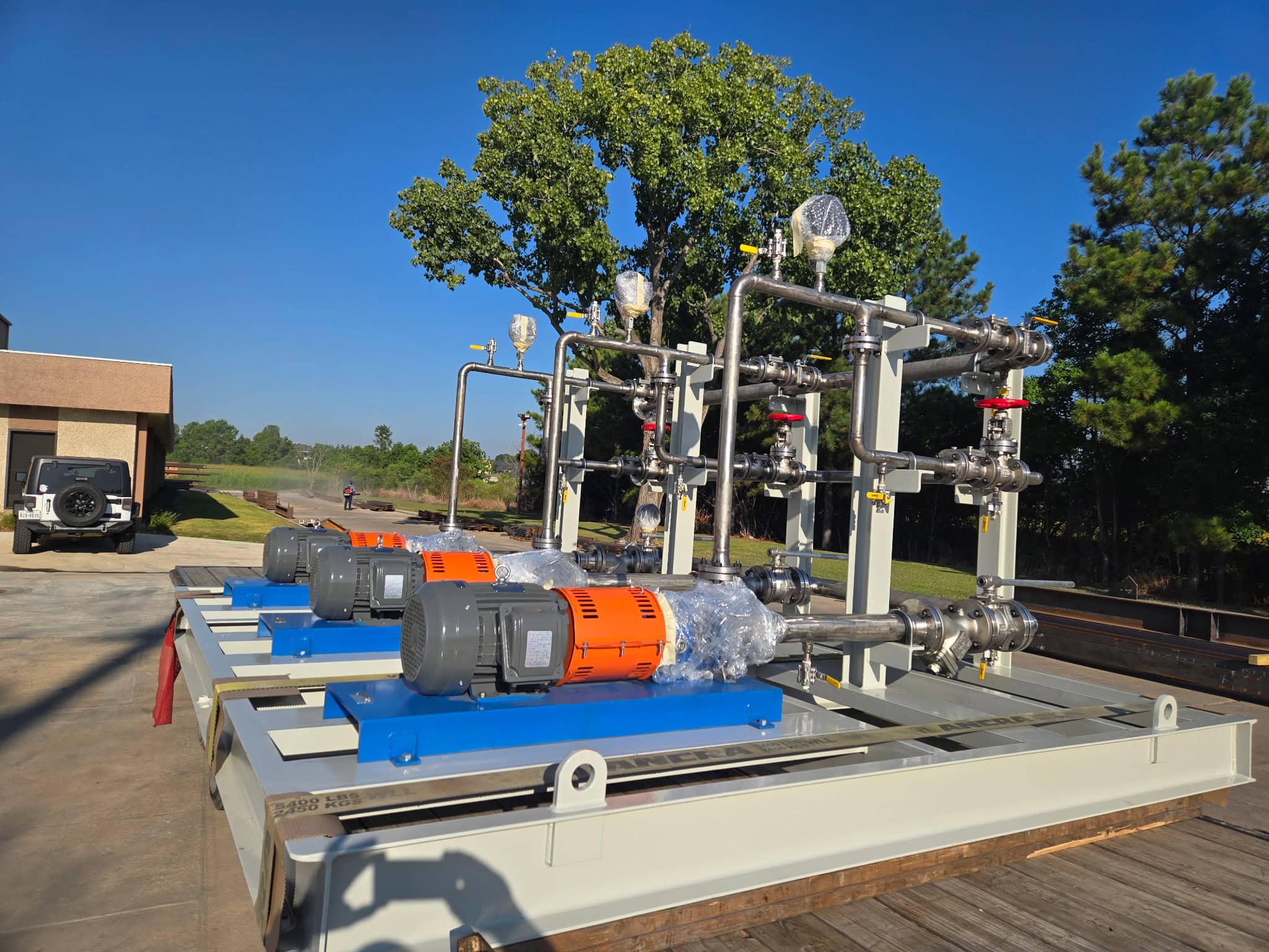 Centrifugal pump skid package with two orange motors on a blue baseplate and stainless steel piping manifold on a painted steel skid outdoors