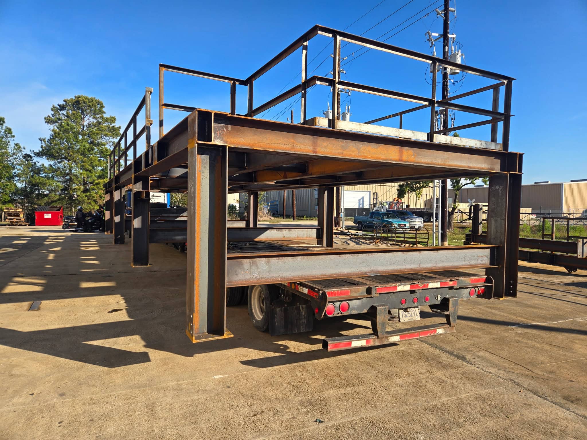 Large welded structural steel skid frame with wide flange beams and handrails loaded on a flatbed trailer outside the WeldIT shop