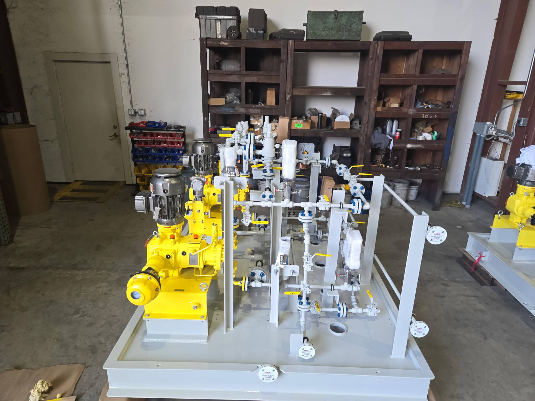 Completed metering pump skid package with yellow pumps, motor and gray stainless steel piping on a painted steel base in the WeldIT fabrication shop