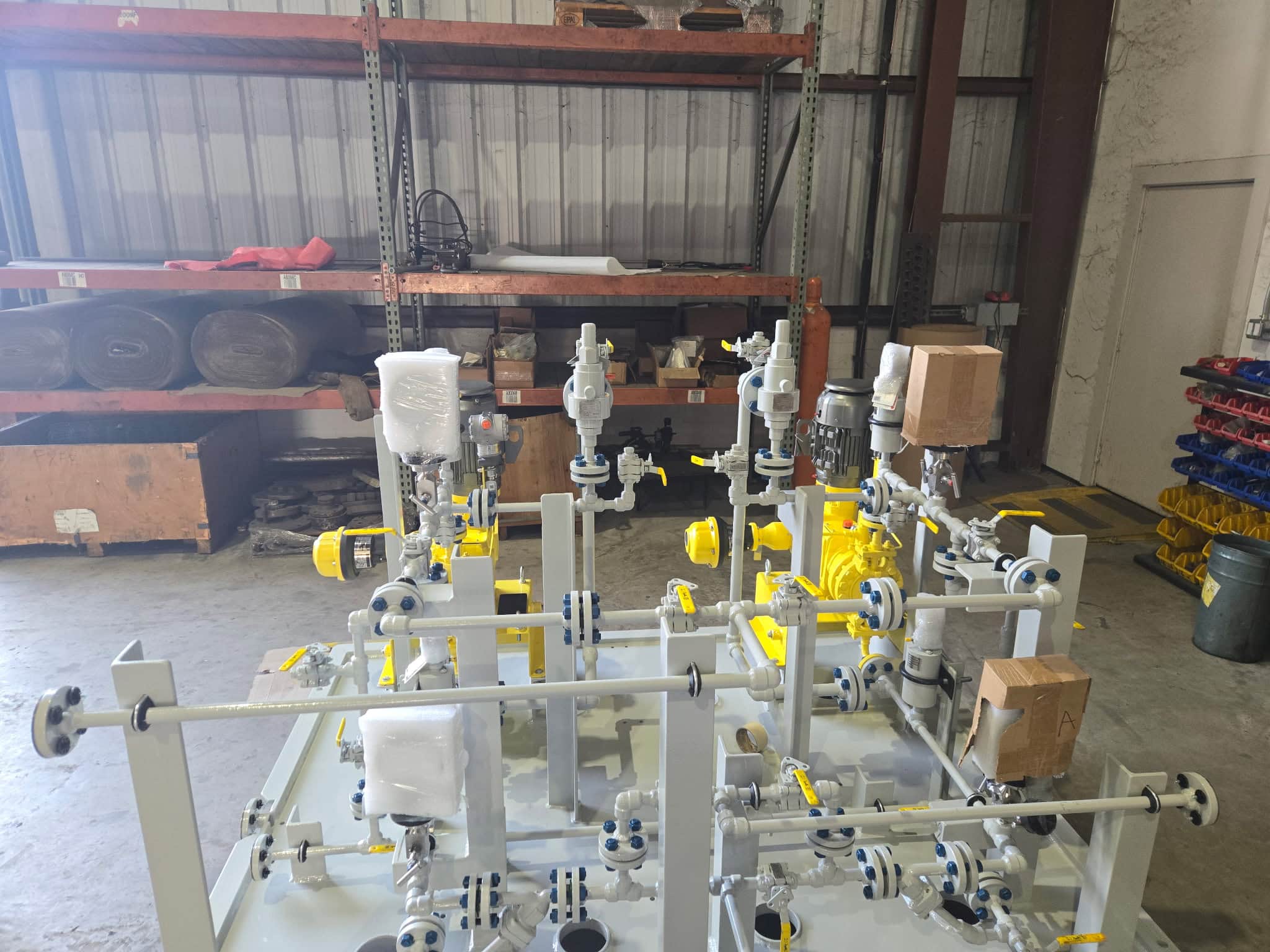 Overhead view of a chemical dosing skid with yellow metering pumps, gray piping manifold and valves on a steel skid base inside a fabrication shop