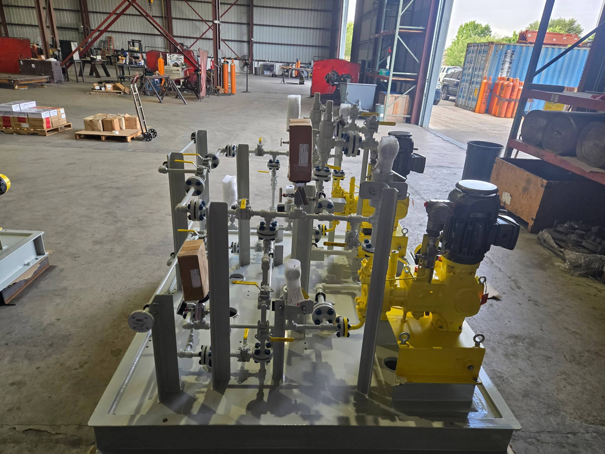 Side view of a chemical injection metering pump skid with stainless steel piping, valves and calibration columns on a painted steel base in the WeldIT shop