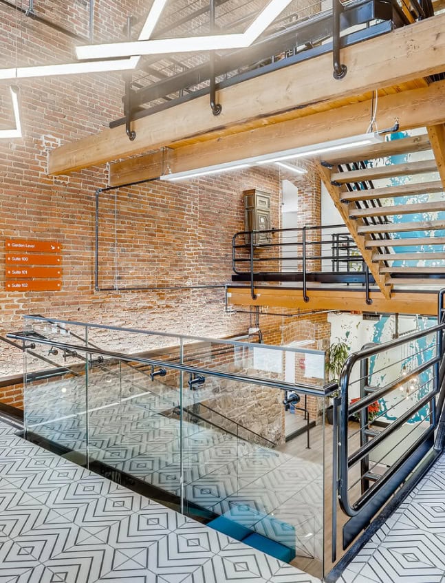 Modern office interior with exposed brick walls, metal handrails, and glass stair railings, showcasing the stylish design of Office Evolution franchising locations.
