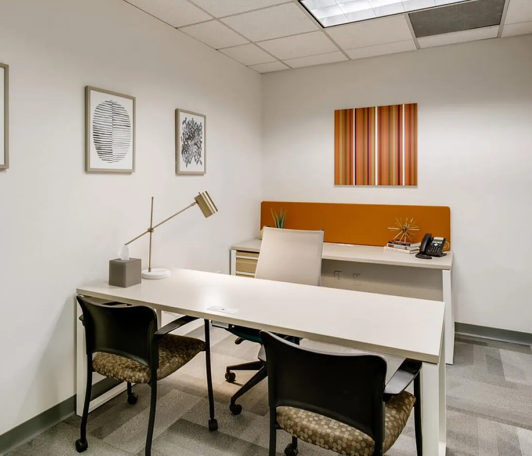Modern office space designed for franchise business meetings, featuring a clean white desk, comfortable chairs, and stylish wall art, ideal for Office Evolution franchising opportunities.