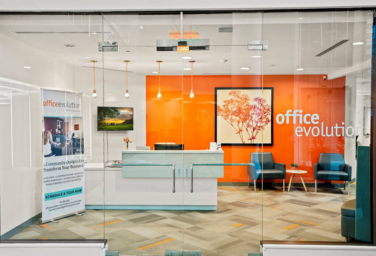Modern Office Evolution franchising center with vibrant orange accent wall, seating area, and reception desk, showcasing a professional environment for business growth and franchise opportunities.