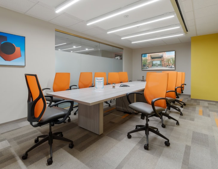 Office Evolution franchising conference room with modern orange and black ergonomic chairs, large meeting table, and digital screens, showcasing professional coworking space solutions.