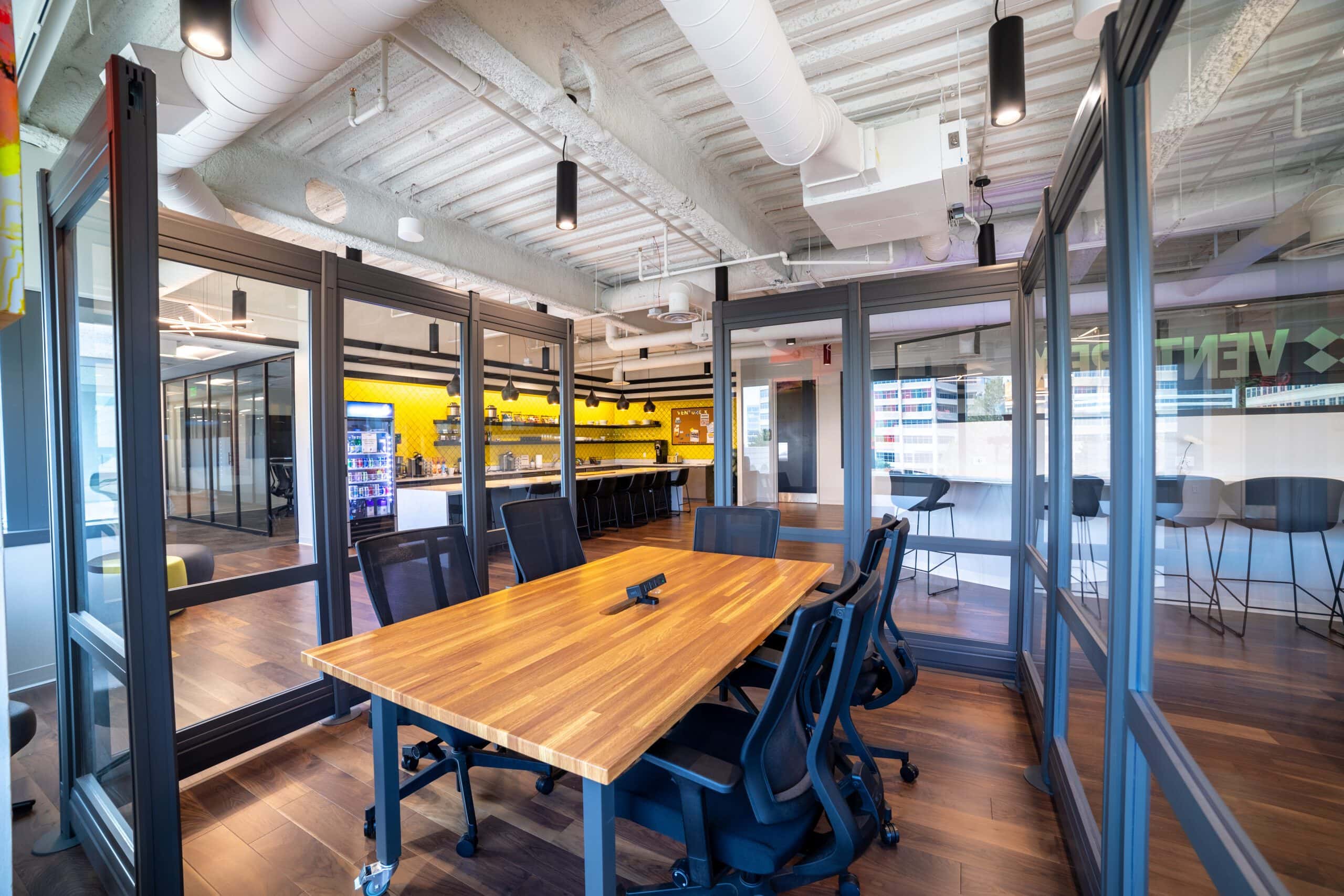 Modern office workspace with glass-enclosed meeting rooms and a conference table, ideal for Office Evolution franchising. Bright, professional environment perfect for business growth and collaboration.