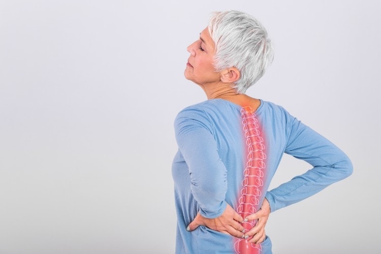 Elderly woman holding painful lower back with spine highlight - One Body LDN Elderly woman holding painful lower back with spine highlight