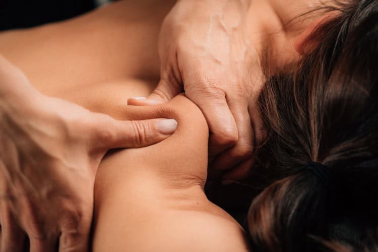 Therapist applying deep tissue pressure on clients shoulder muscle - One Body LDN Therapist applying deep tissue pressure on client’s shoulder muscle