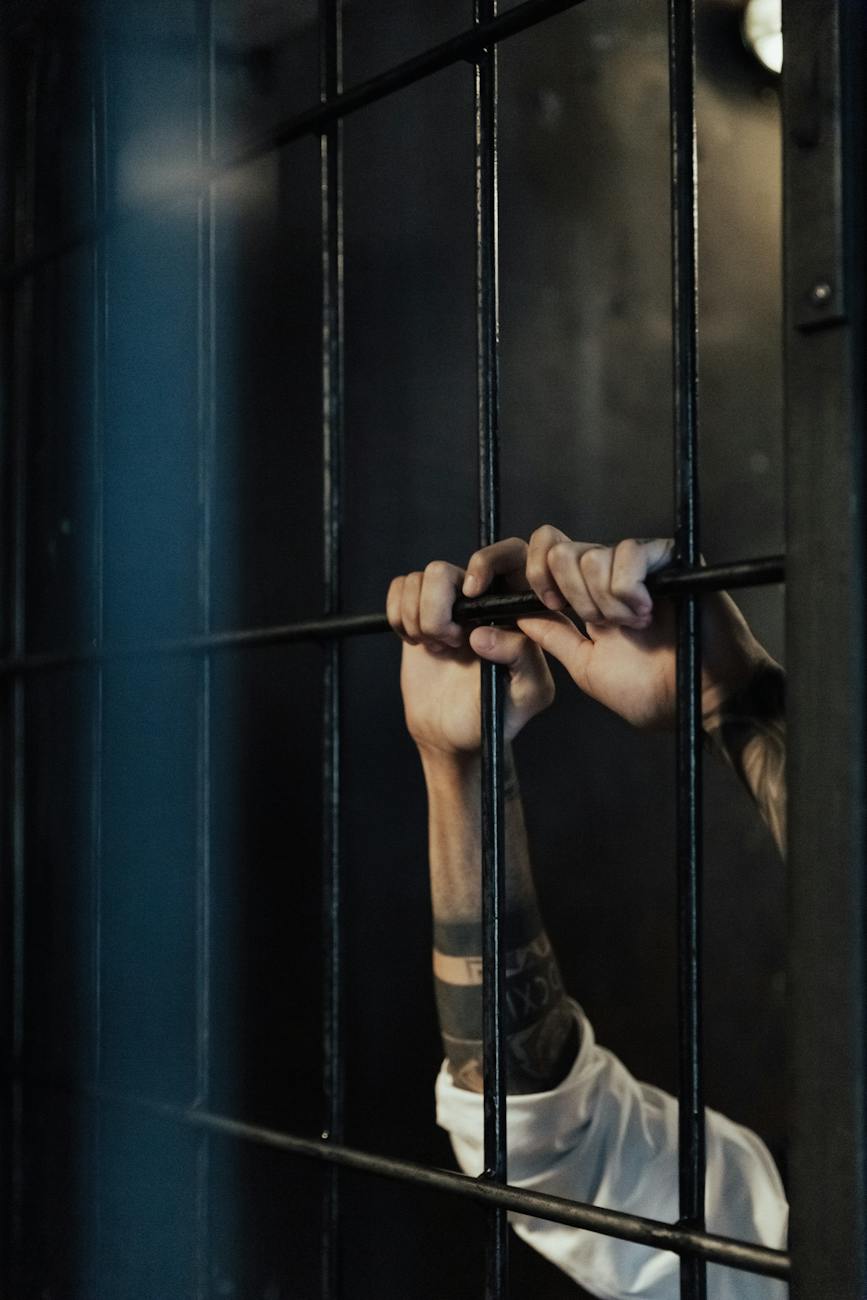 A prisoner grasps at the bars of his cell