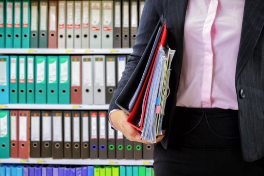 businesswoman-holding-data-files-binder-shelves-background-min