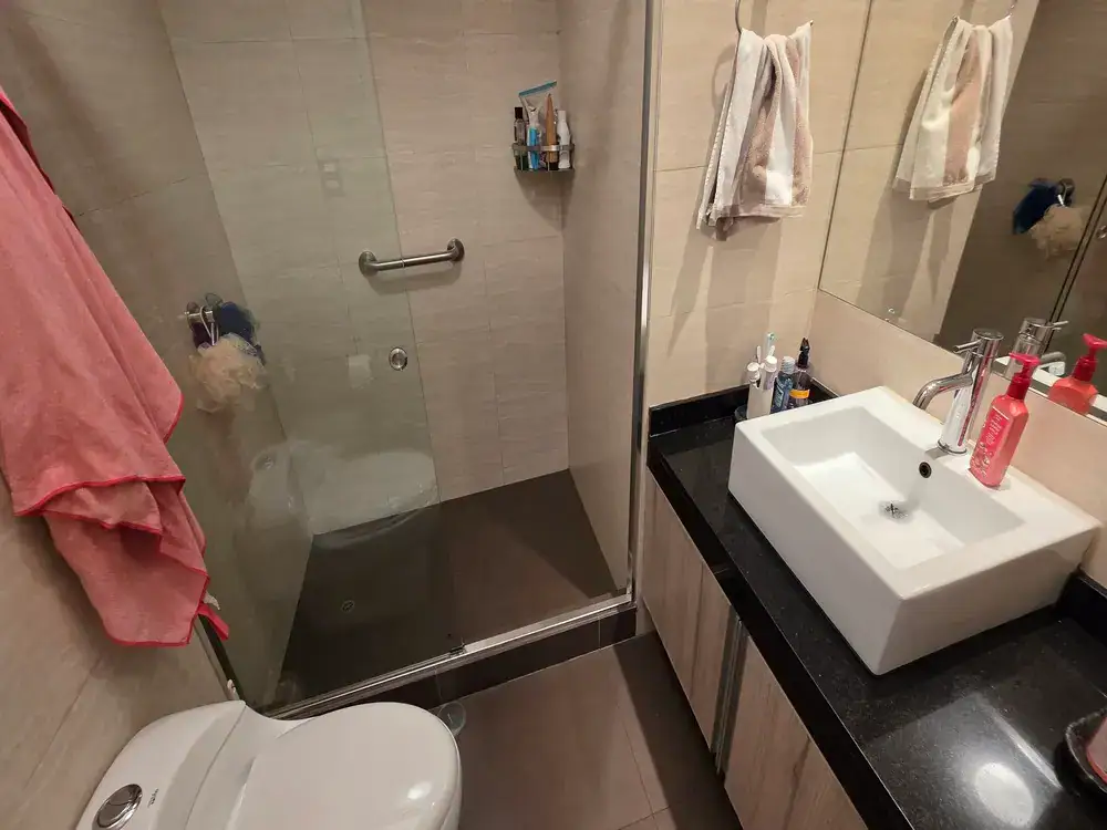 Modern bathroom with a glass shower enclosure, a white square basin sink on a black countertop, and a toilet nearby.