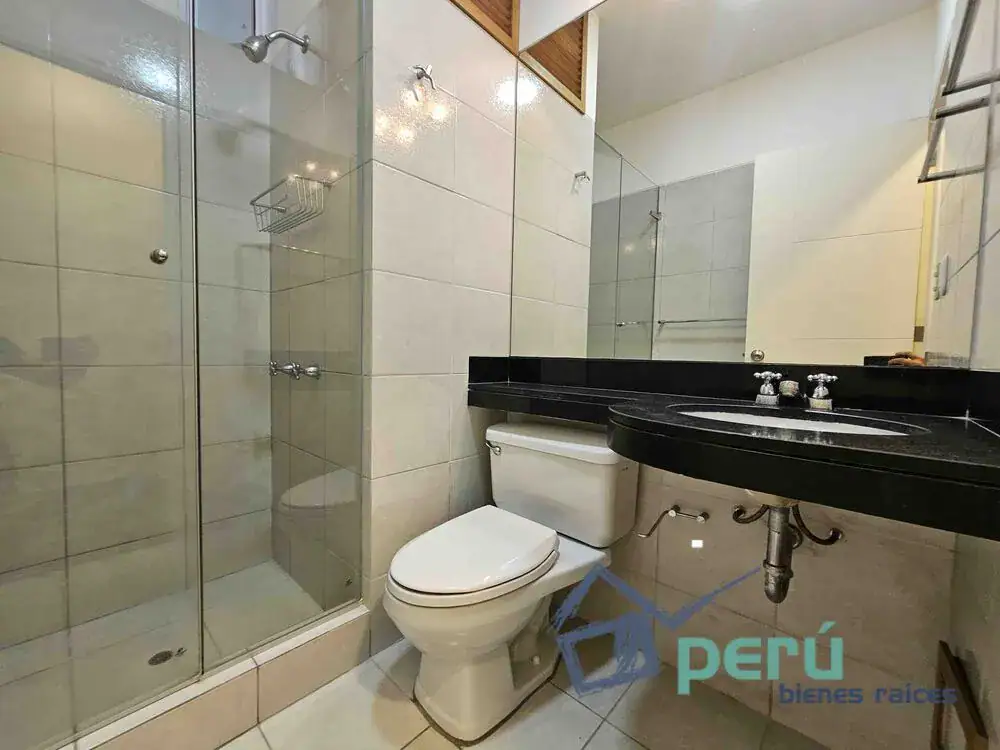 Bathroom with glass shower enclosure, white toilet, and a black granite counter with an oval sink beneath a large mirror.
