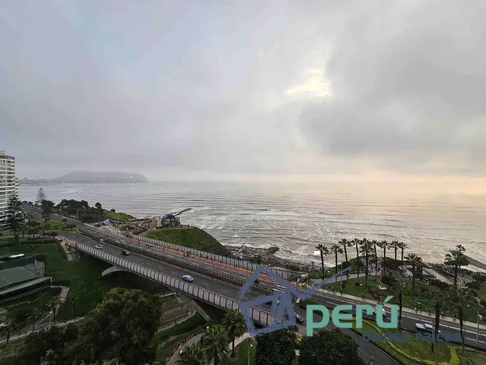 Coastal highway and pedestrian bridge along the shore, with palm trees, ocean waves, and sunset light in Peru. (watermark visible)