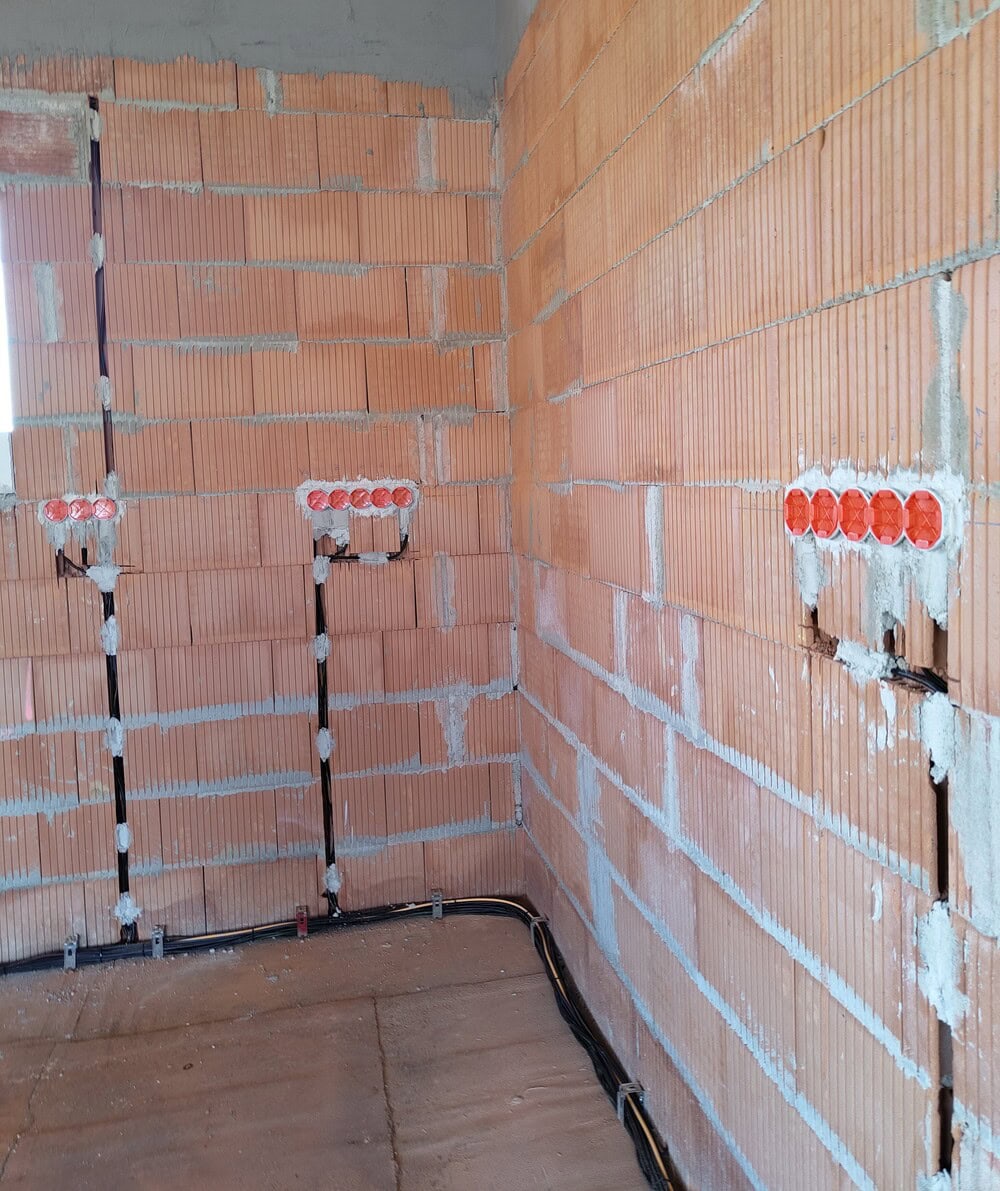 Hrubé rozvody elektroinstalace v novostavbě s vysekanými drážkami a osazenými krabicemi pro zásuvky a vypínače.