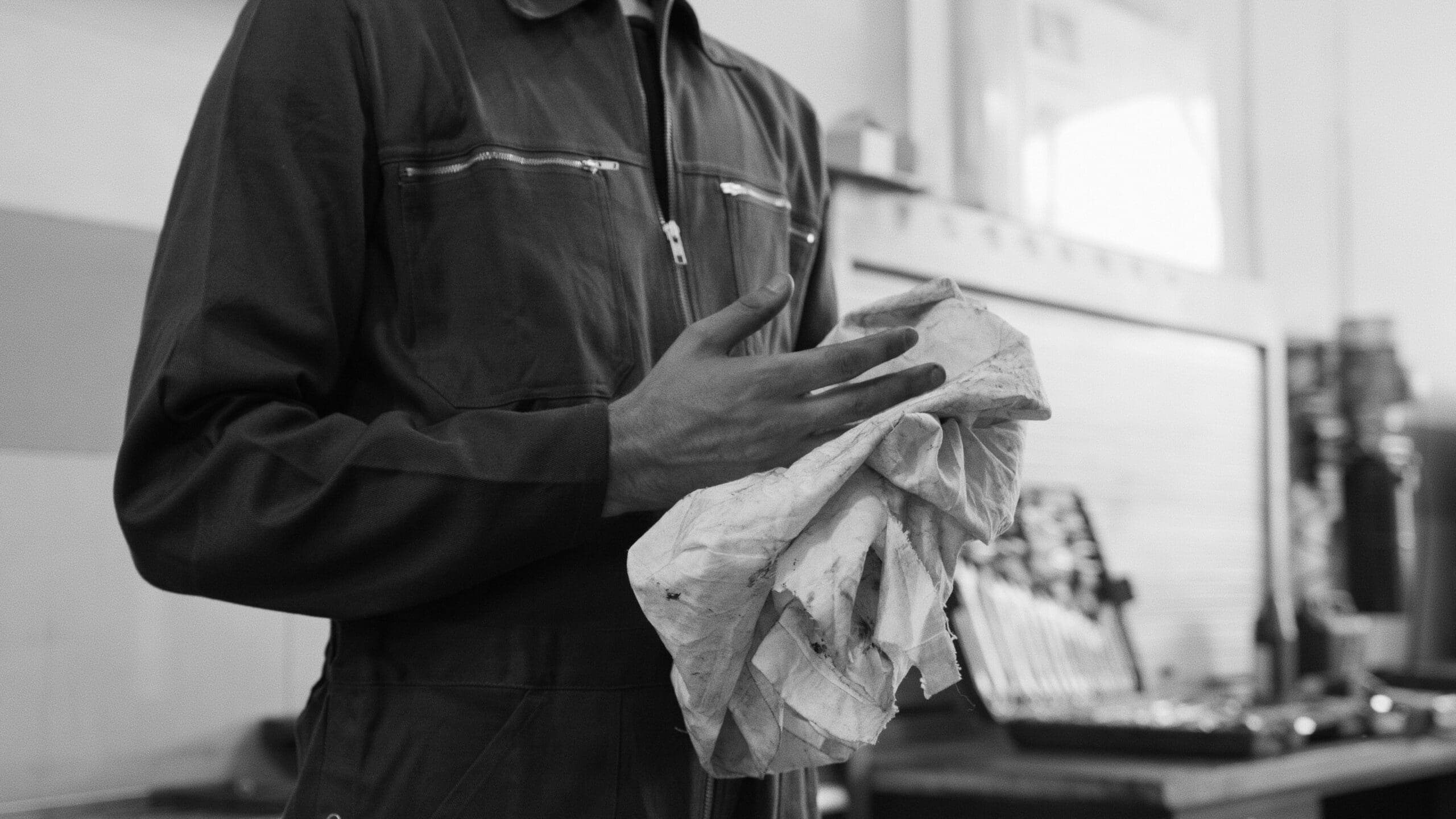 Mechanic cleaning hands with cloth in a monochrome automotive workshop setting.