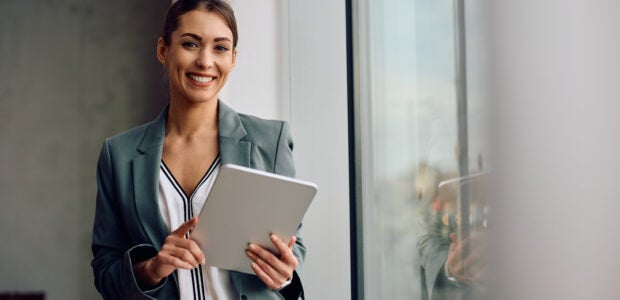 Happy businesswoman working on digital tablet in the office and looking at camera.