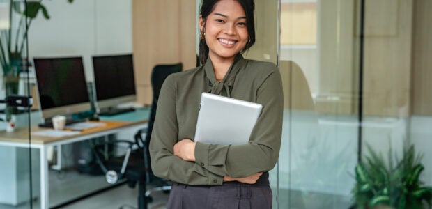 Filipino woman stands in modern office with tablet in hand while smiling and showing confidence during work hours