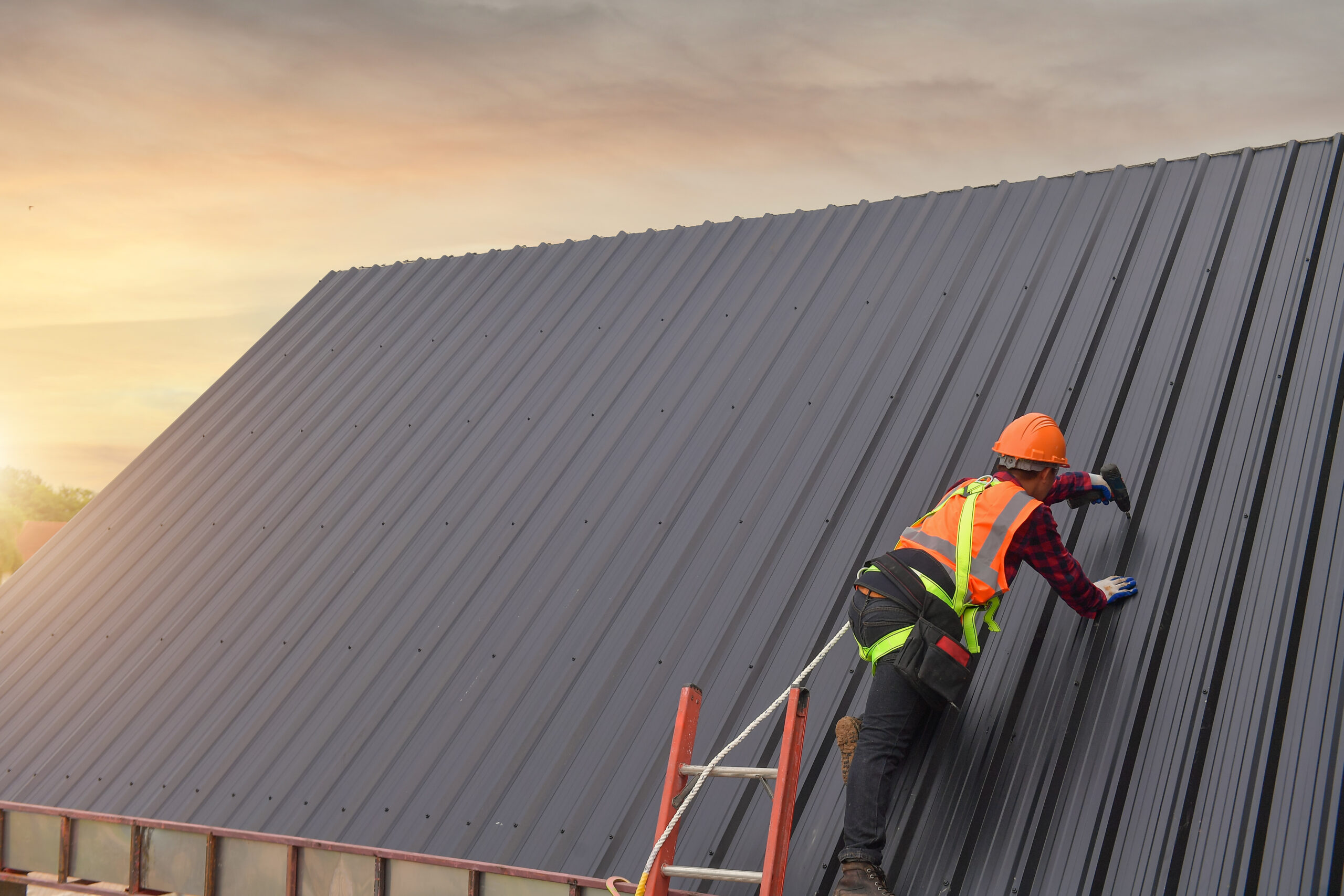 A roofer installing a metal roof during sunset