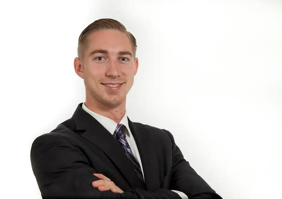 A Safe Pacific Financial advisor, dressed in a dark suit and striped tie, stands confidently with arms crossed and a welcoming smile against a plain white background, representing expert wealth management guidance, the infinite banking strategy, financial advice tailored for affluent Canadian families, and bespoke life insurance solutions.