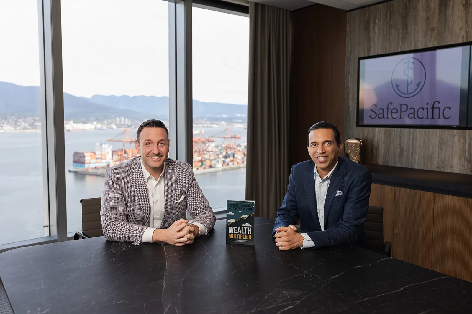 Two executives discuss wealth management and infinite banking at a Safe Pacific Financial meeting, life insurance book on table.