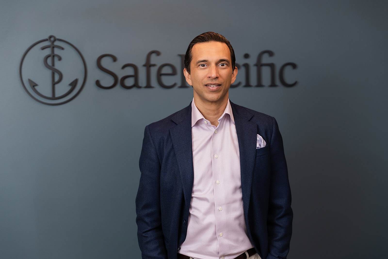 A man in a navy blazer stands before the Safe Pacific Financial wall, symbolizing bespoke Canadian wealth management and infinite banking.