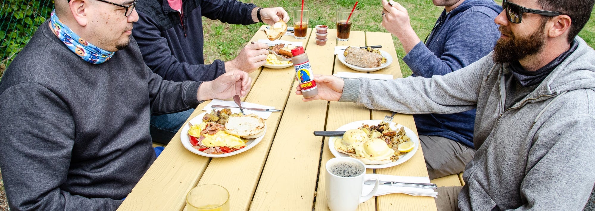 People sitting at a picnic table eating food. One is holding secret aardvark habanero sauce