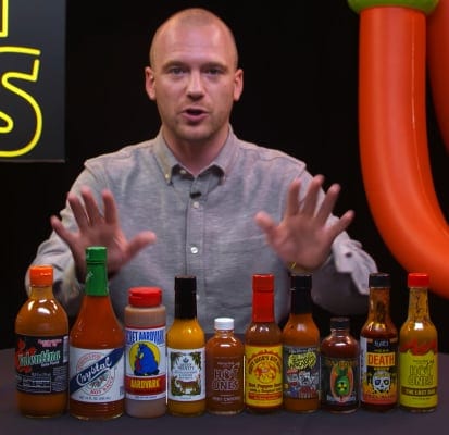 Person standing behind various hot sauces with hands up
