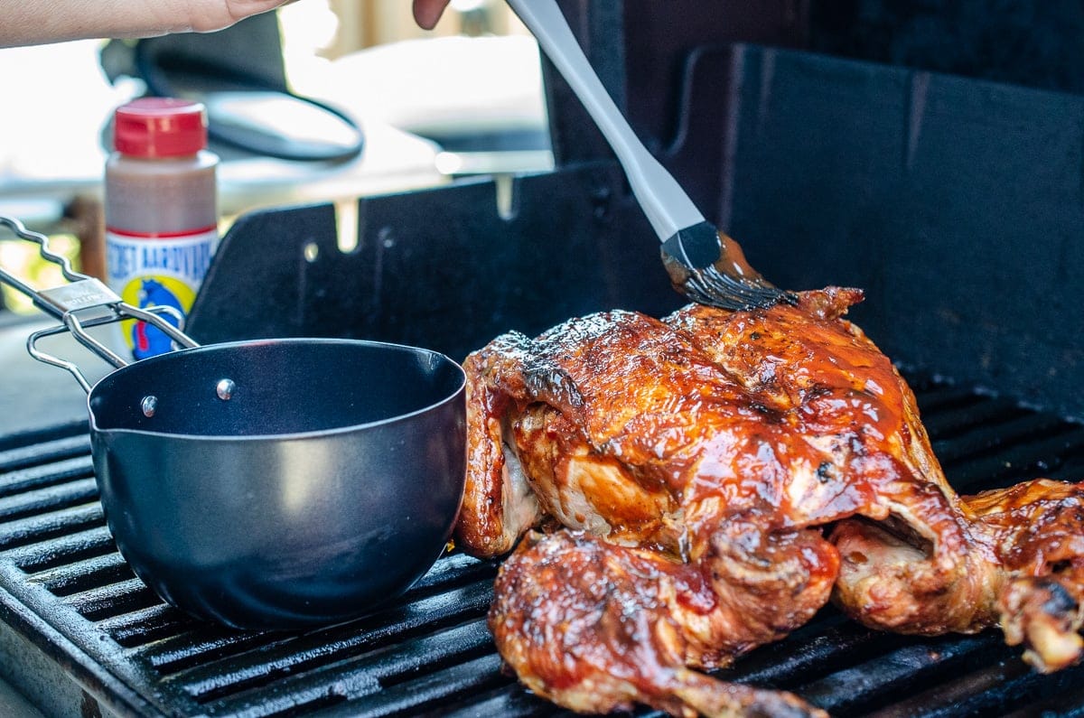 image of opened grill with whole chiken and bowl of sauce. A brush is placing sauce on chicken