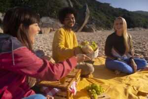 Drei Menschen sitzen gemeinsam auf einer Decke im Park und unterhalten sich.