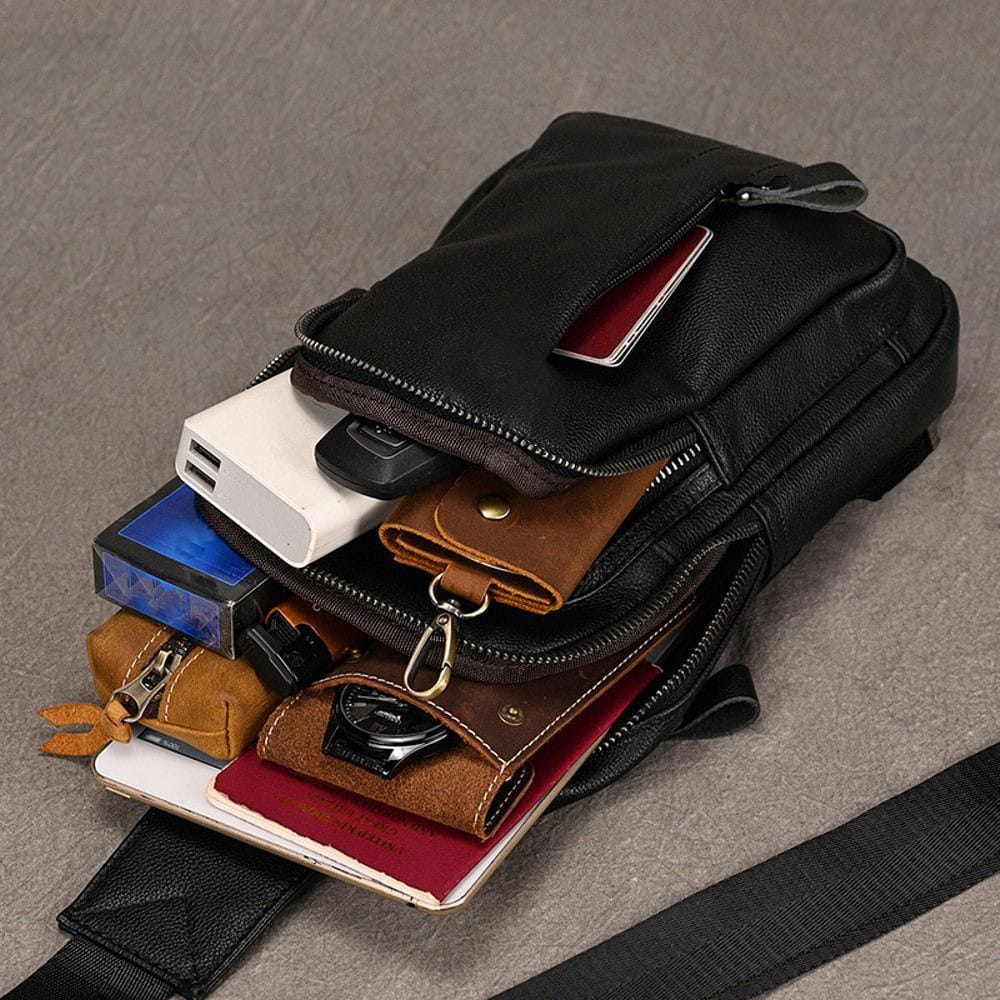 Black leather sling bag with multiple compartments and accessories inside.