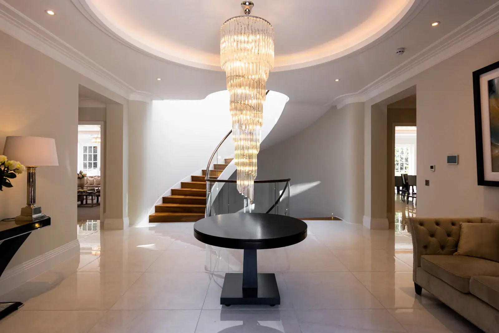 Entrance foyer with spiral chandelier and marble floor in a Cobham home with smart lighting