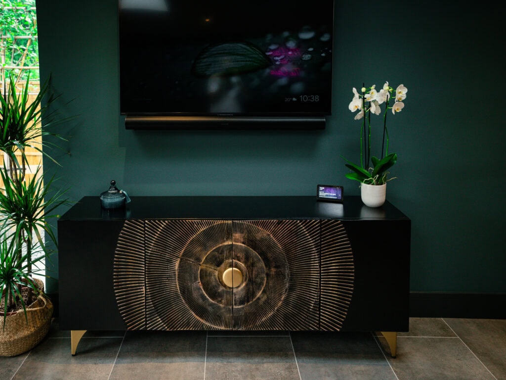Garden room lounge with wall-mounted TV above a carved black sideboard