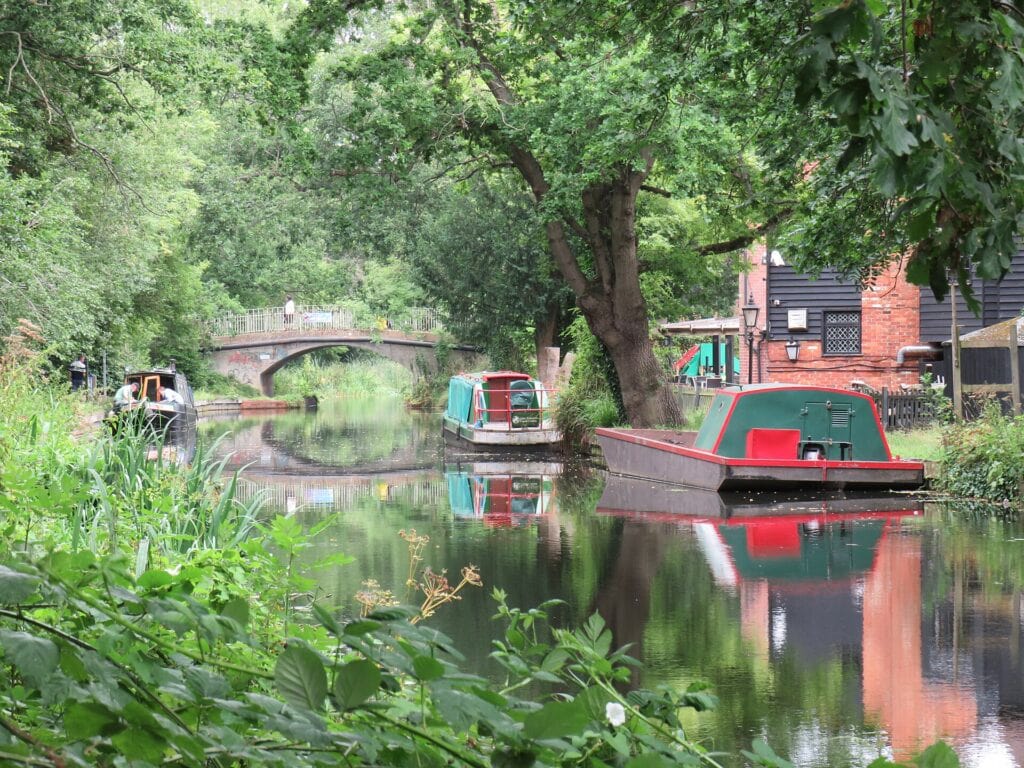 Narrowboats moored on the Basingstoke Canal in Woking, with a brick road bridge beyond. Photo: Richard Rogerson, CC BY-SA 2.0