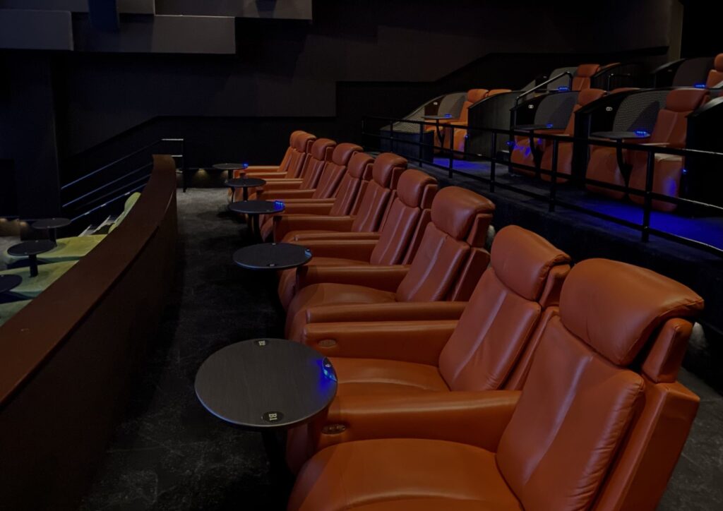 Rows of tan leather reclining seats with side tables, the rear rows raised on a stepped riser