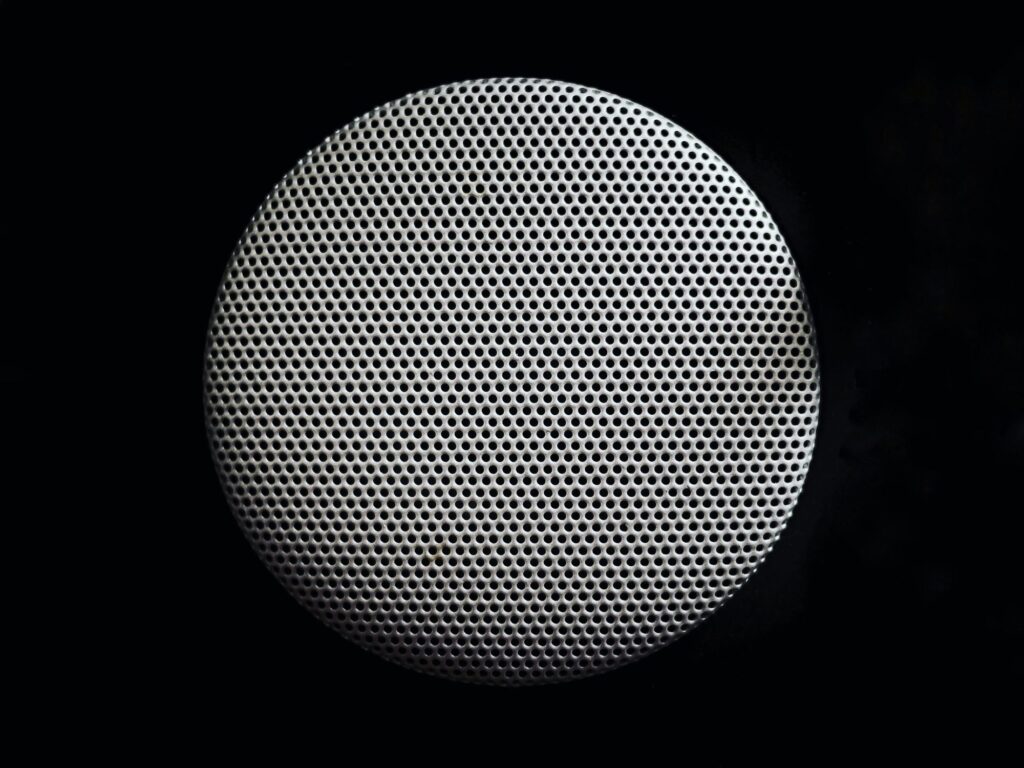 Close-up of a round perforated metal speaker grille against a black background