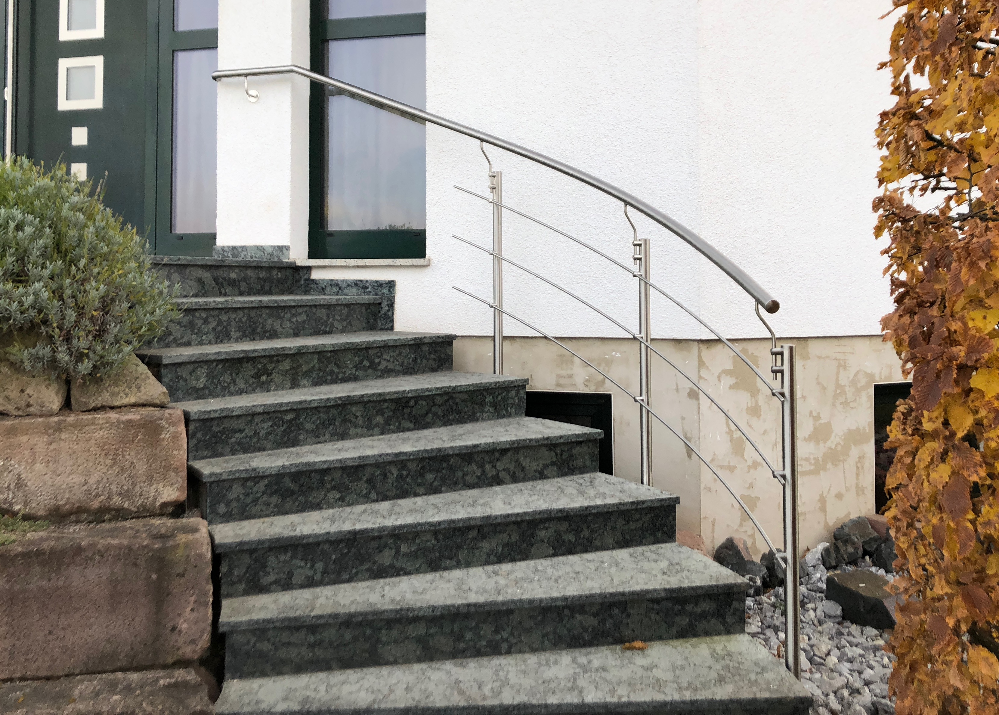Modernes Edelstahlgeländer mit gebogenem Handlauf und waagerechten Stäben an einer Granittreppe, Geländer von Stahl- und Metallbau Drost.