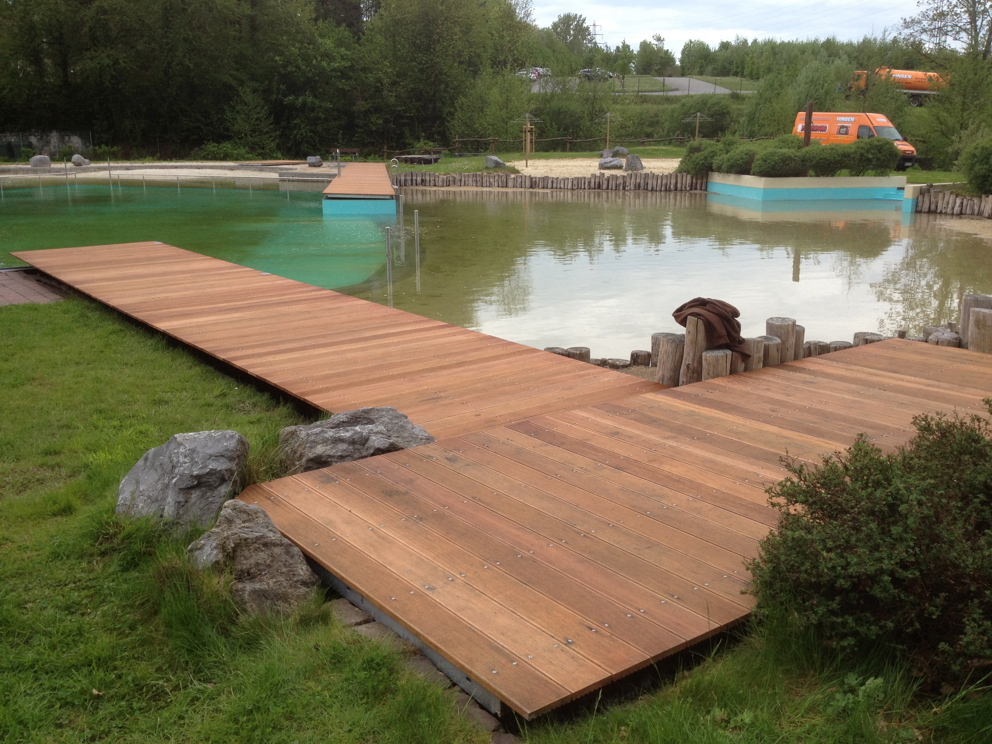 Weitläufige Holzterrasse und Stege führen über eine grüne Wiese zu einem Naturteich, ein maßgefertigtes Projekt von Stahl- und Metallbau Drost.