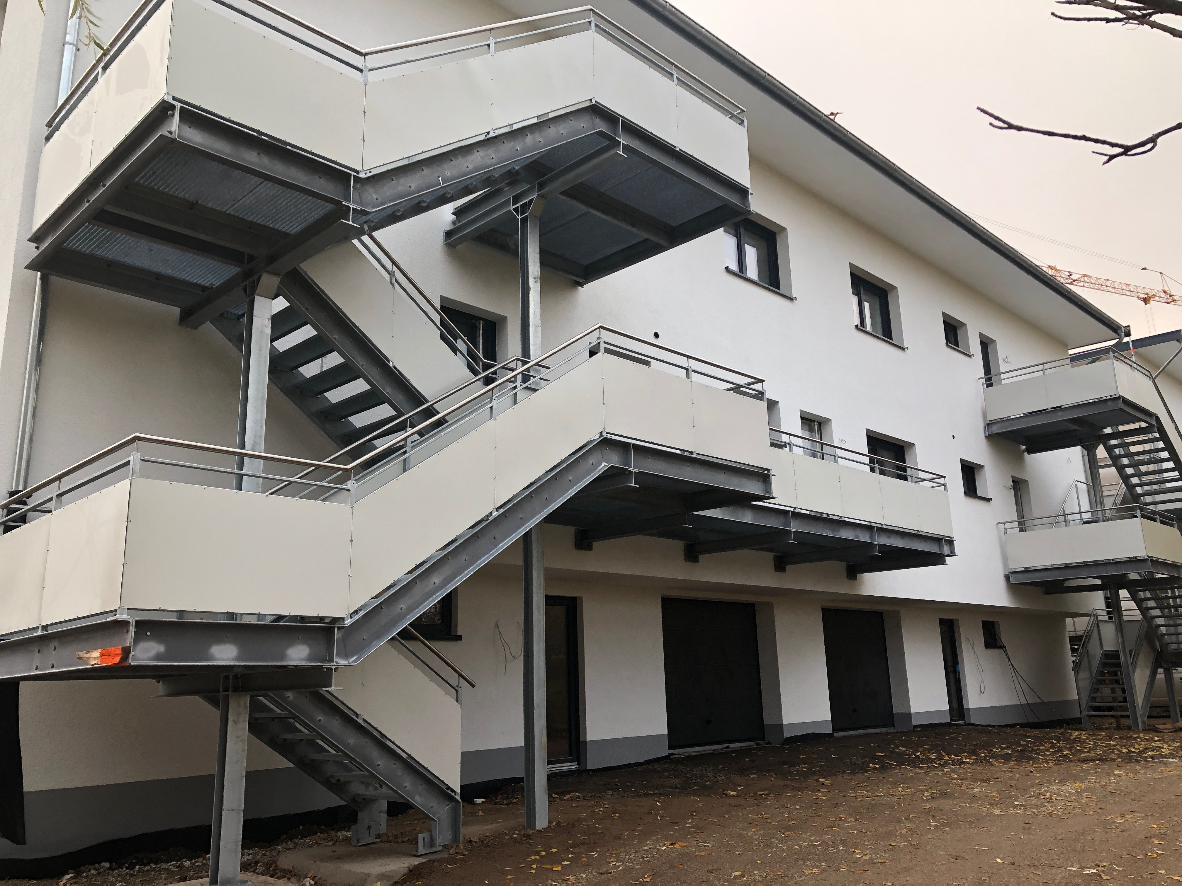Robuste Außentreppe aus verzinktem Stahl mit hellen Paneel-Brüstungen, von Stahl- und Metallbau Drost, an einem mehrstöckigen weißen Gebäude.
