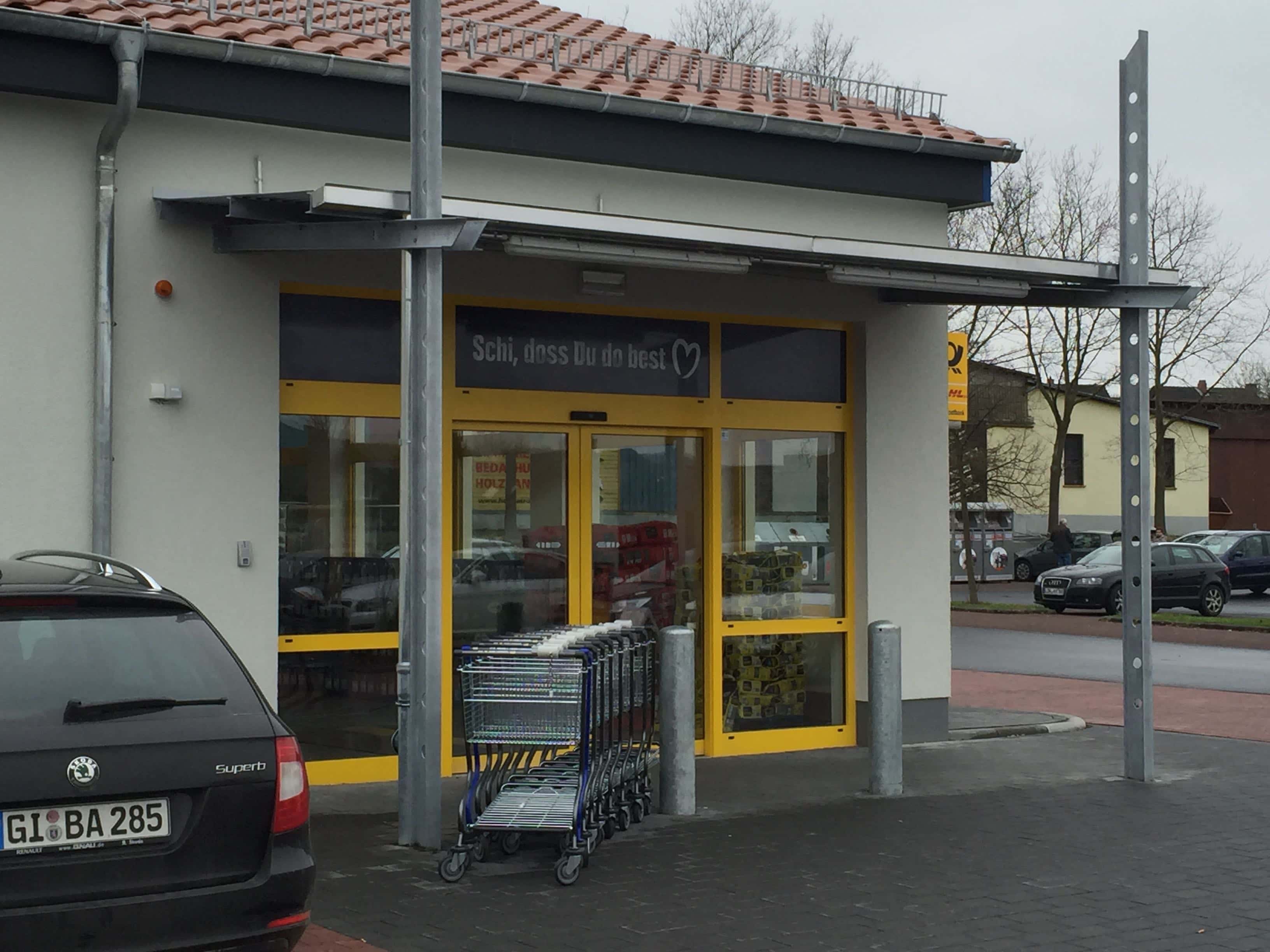 Modernes, flaches Metallvordach von Stahl- und Metallbau Drost über dem Eingang eines Geschäfts, mit seitlicher Stütze aus Metall.