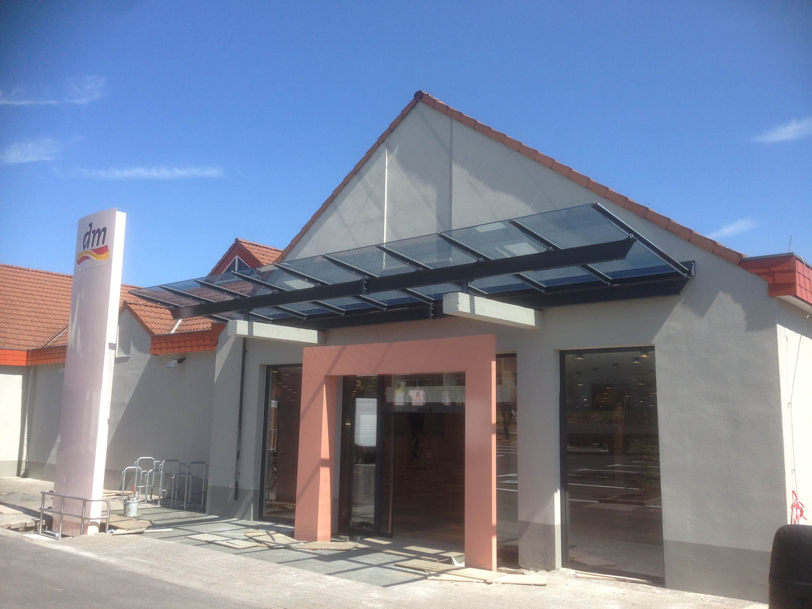 Modernes Glas- und Metallvordach am Eingang eines dm-Marktes, gefertigt von Stahl- und Metallbau Drost.