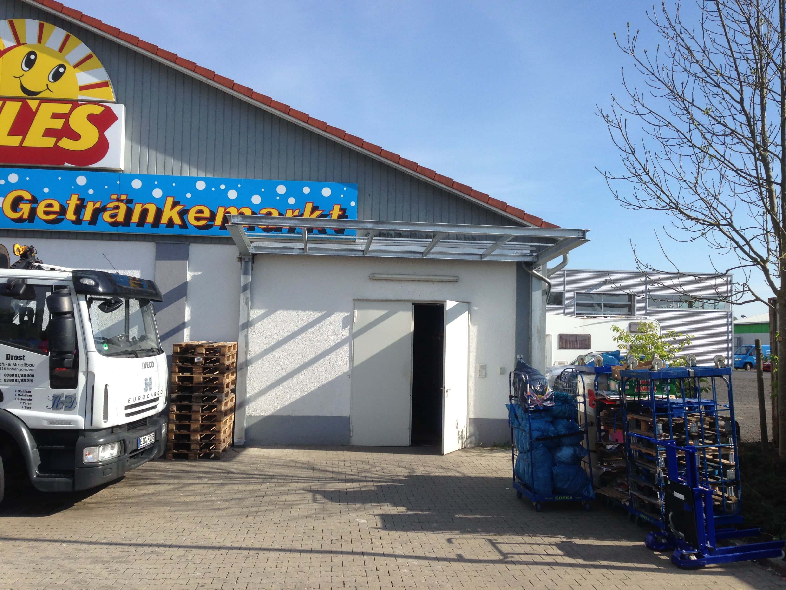 Ein robustes Vordach aus verzinktem Stahl von Stahl- und Metallbau Drost über dem Eingang eines Gewerbegebäudes, links daneben ein Lastwagen und gestapelte Paletten.