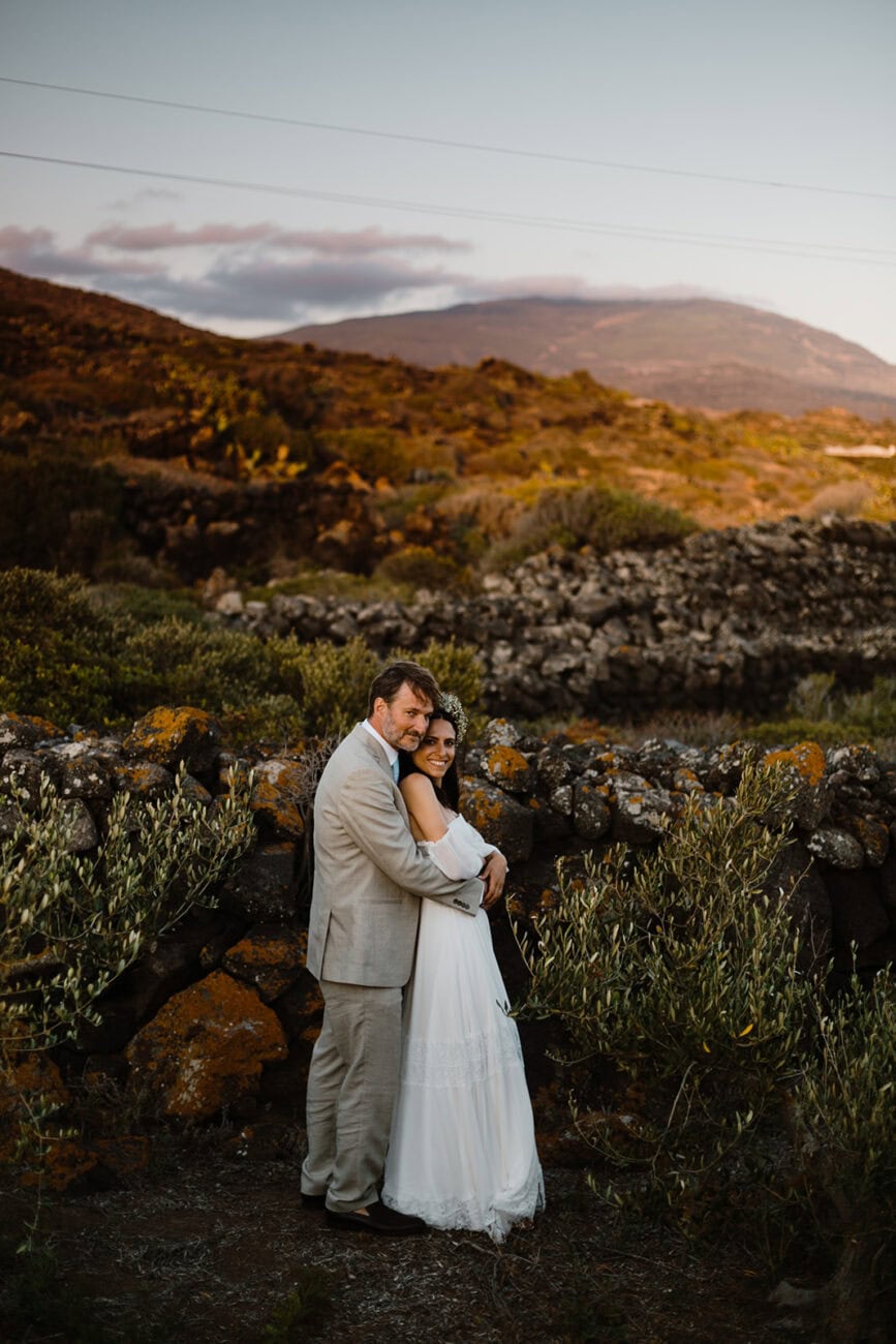 Bride and groom standing together on a hillside overlooking the Mediterranean coast at sunset