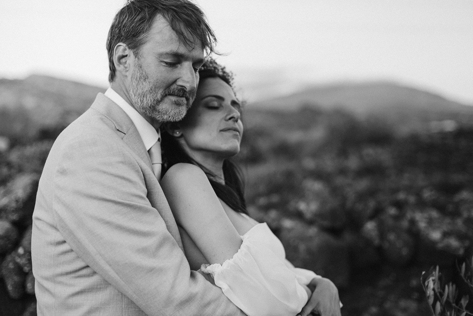 Black and white photo of a groom embracing his bride outdoors at golden hour during their Italy wedding