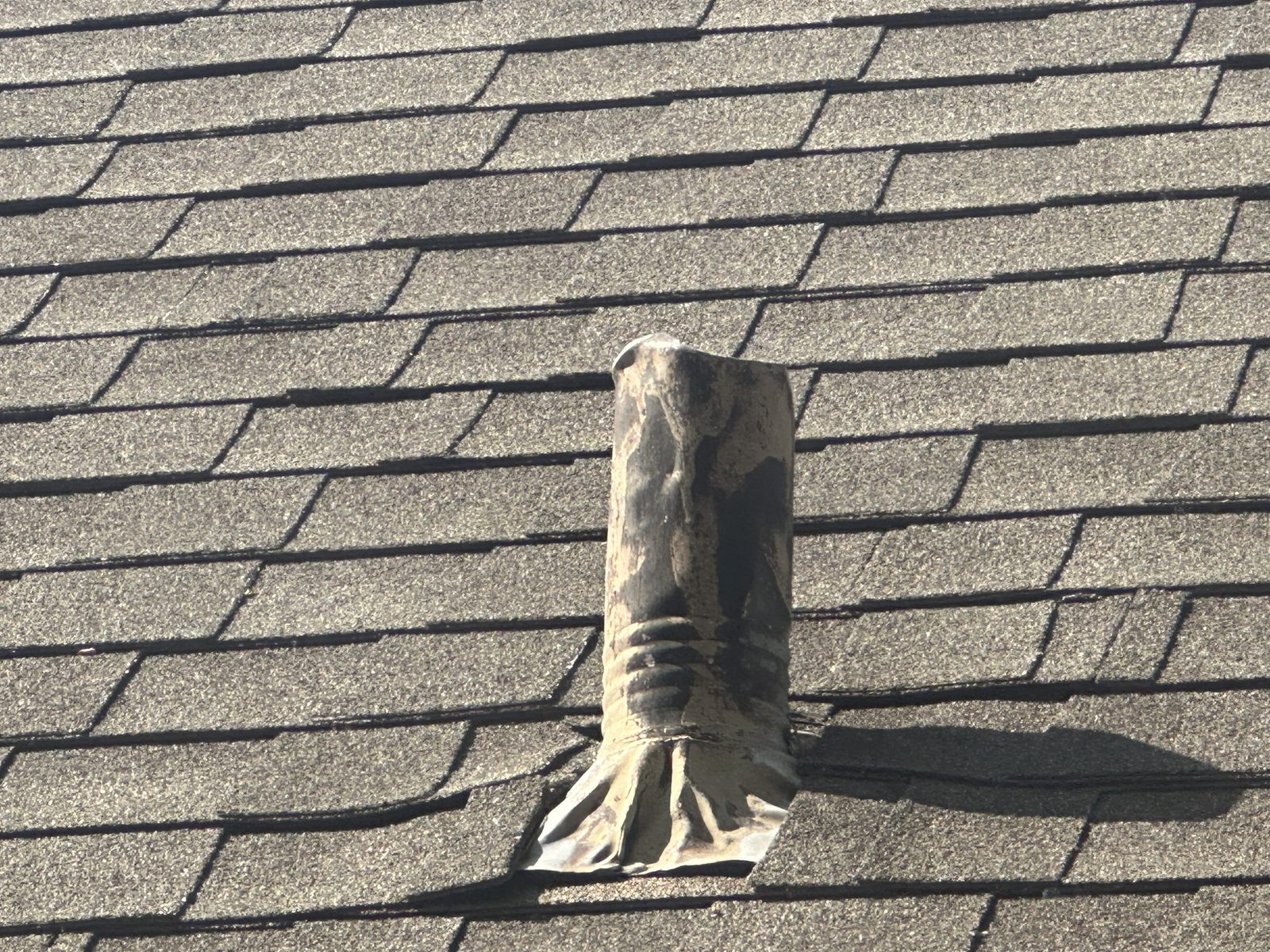 Damaged asphalt shingles around a vent pipe on the roof.