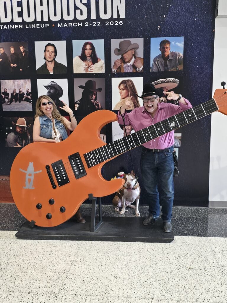 Adam H. Miller, The Texas Bulldog, and Houston's LaLa posing with a giant guitar display and a dog at RodeoHouston 2026
